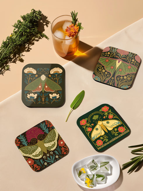 A set of four square hardboard coasters with smoothly rounded corners and a protective high-gloss finish. Each coaster features a unique, highly detailed Art Nouveau style illustration of a moth centered against a dark, botanical background. The intricate artwork uses a rich, moody color palette of deep forest greens, ochre, muted olive, crimson, and black, evoking a vintage, scholarly feel. These decorative drinkware accessories are designed for coffee table and bar cart use.